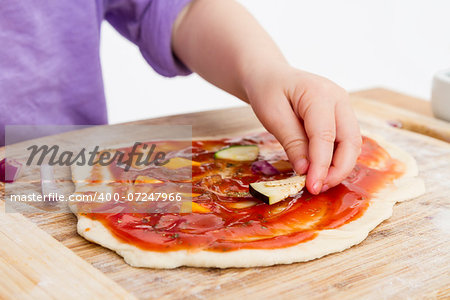 hand of young child making pizza on wooden board