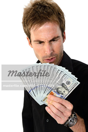 A young handsome man holding a lot of new hundred dollar bills isolated on white background.  He is staring at the money with a look of disbelief.  This newly redesigned US currency was released for circulation in October of 2013.