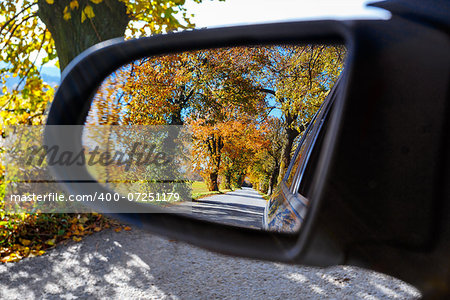 rural road in the autumn with yellow colored trees reflected in car mirror