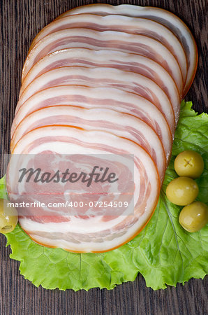 Slices of Delicious Smoked Ham Roll with Lettuce and Green Olives closeup on Wooden background