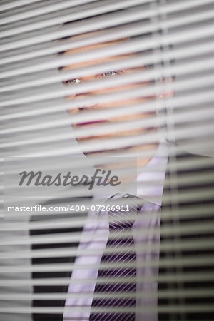 Handsome serious young businessman peeking through blinds in the office