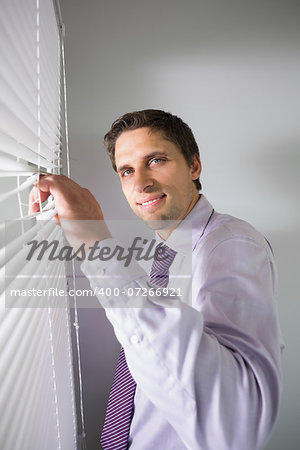 Portrait of a young businessman peeking through blinds in the office