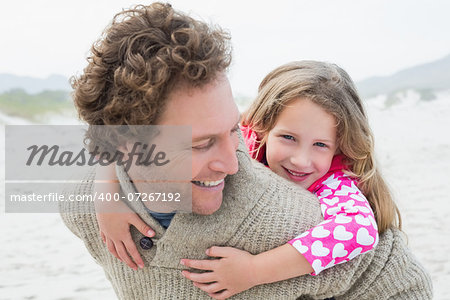 Happy man piggybacking his cheerful daughter at the beach