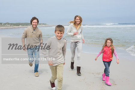 Full length portrait of a happy family of four running at the beach