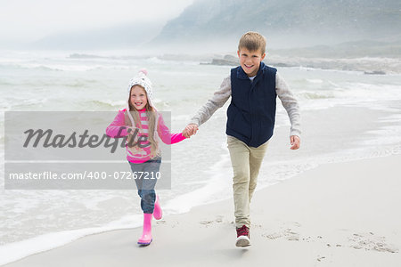 Full length of a happy brother and sister walking hand in hand at the beach