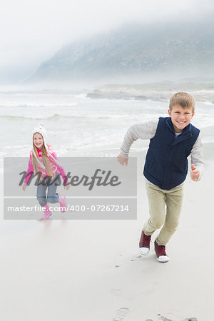 Full length portrait of a happy brother and sister running at the beach