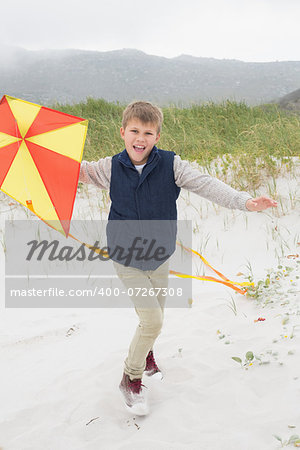 Full length portrait of a cheerful young boy with kite at the beach