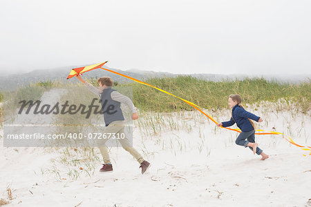 Full length side view of cheerful kids running with kite at the beach