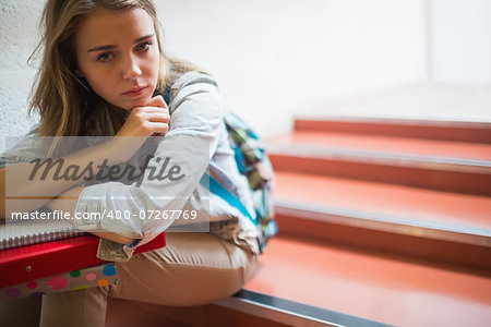 Sad lonely student sitting on stairs looking at camera in college