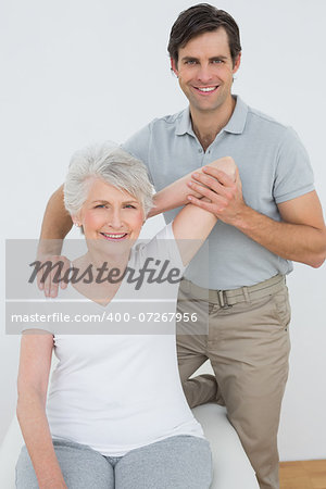 Male physiotherapist stretching a smiling senior woman's arm in the medical office