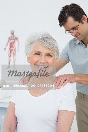 Male physiotherapist massaging a senior woman's shoulders in the medical office