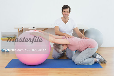 Portrait of a physical therapist assisting senior woman with yoga ball in the gym at hospital