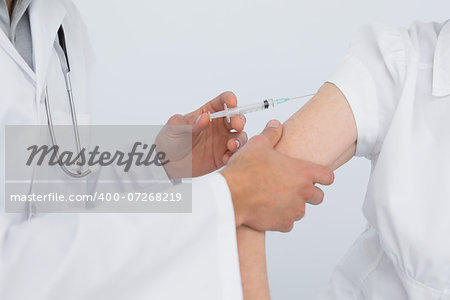 Close-up of hands injecting a female patient's arm over white background