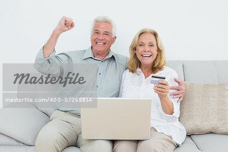 Cheerful senior couple doing online shopping through laptop and credit card on sofa in a house