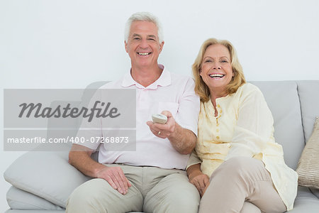 Portrait of a relaxed cheerful senior couple watching television in a house