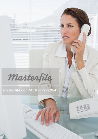 Concentrated young businesswoman using computer and phone at office desk