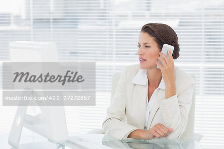 Concentrated young businesswoman using computer and cellphone at office desk