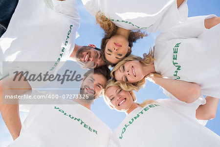 Low angle portrait of happy volunteers forming a huddle against blue sky