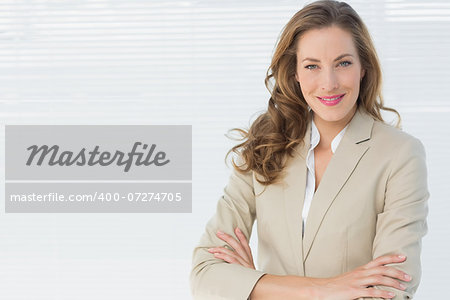 Portrait of a smiling young businesswoman standing with arms crossed against blinds in office