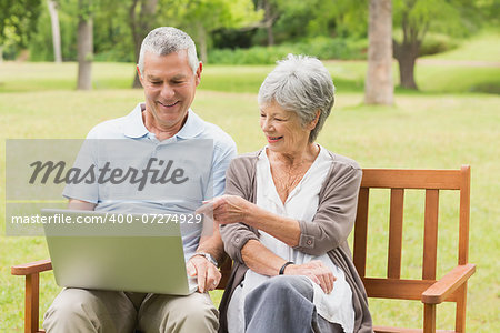 Smiling senior woman and man using laptop on bench at the park