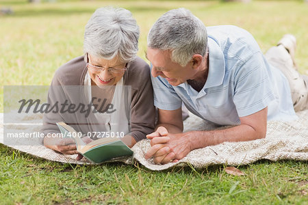 Smiling relaxed senior couple reading book while lying in the park