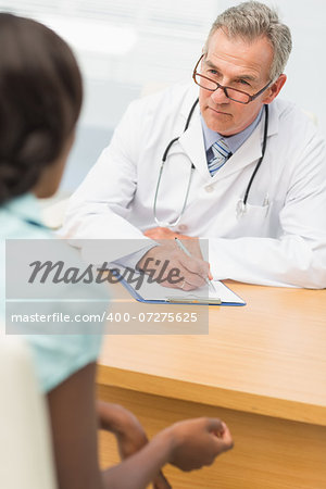 Serious doctor listening to his patient and taking notes in his office at the hospital