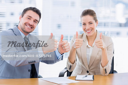 Portrait of smartly dressed businessman and woman gesturing thumbs up at office desk