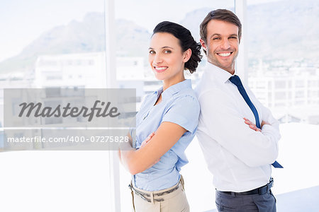 Portrait of a smiling young business couple standing with arms crossed in a bright office