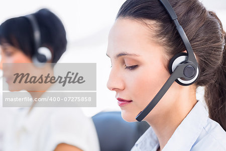 Closeup side view of a beautiful young female executive with headset in a bright office