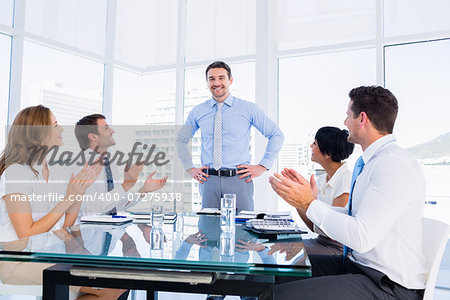 Business executives clapping around conference table in a bright office