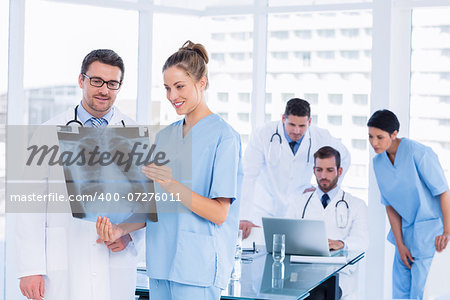 Smiling doctors examining xray with colleagues using laptop behind in a medical office