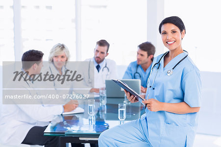 Smiling female surgeon holding reports with colleagues in meeting at a medical office
