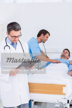 Doctor writing reports with patient and surgeon in background at the hospital