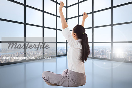 Businesswoman sitting cross legged cheering against room with large windows showing city