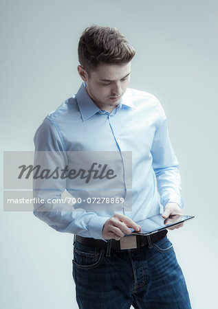 Young man looking down at tablet computer, studio shot on white background