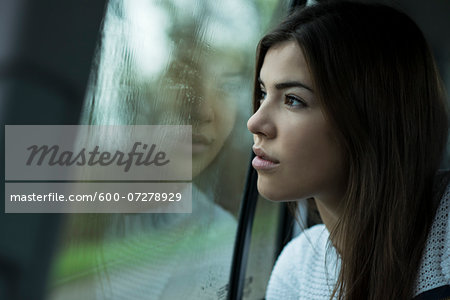 Portrait of young woman sitting inside car and looking out of window and day dreaming on overcast day, Germany