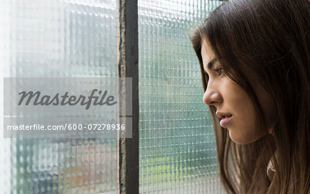 Close-up portrait of young woman day dreaming and looking out window, Germany