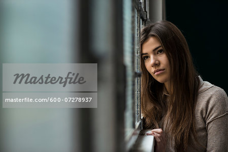 Portrait of young woman standing in front of window, day dreaming and looking into the distance, Germany