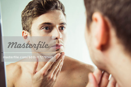 Close-up of young man looking at reflection in bathroom mirror, studio shot