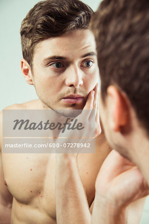 Close-up of young man looking at reflection in bathroom mirror, studio shot
