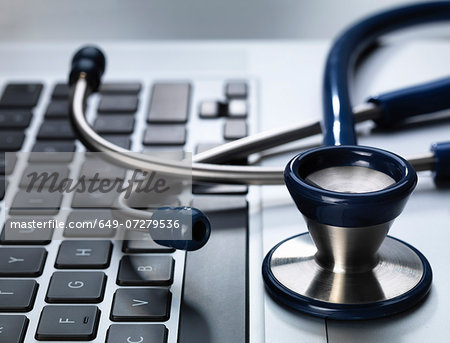 Stethoscope sitting on laptop illustrating online healthcare and doctor's desk