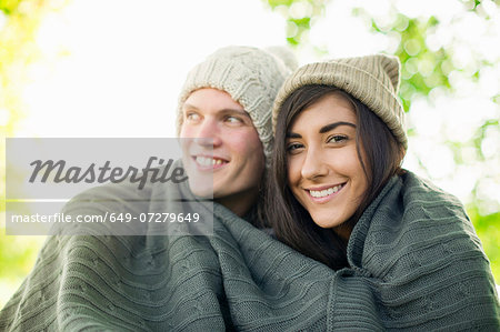 Young couple wearing knit hats wrapped in blanket