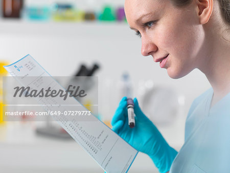 Technician holding blood sample in clinical laboratory with test results