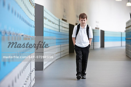 Unhappy schoolboy walking alone in school corridor