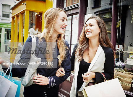 Young women walking down street carrying shopping bags and laughing