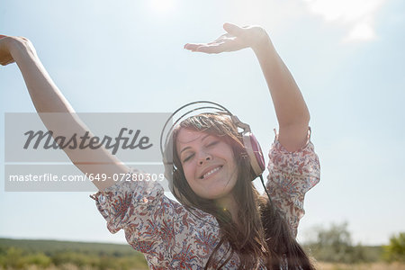 Portrait of mid adult woman dancing in field wearing headphones with arms raised
