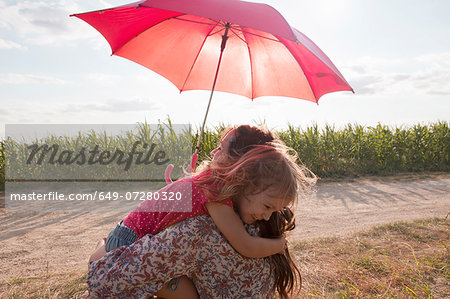 Mother and daughter hugging under red umbrella