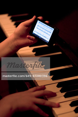 Close up of hands using smartphone whilst playing piano