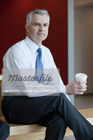 Businessman in waiting area of office, with hot drink