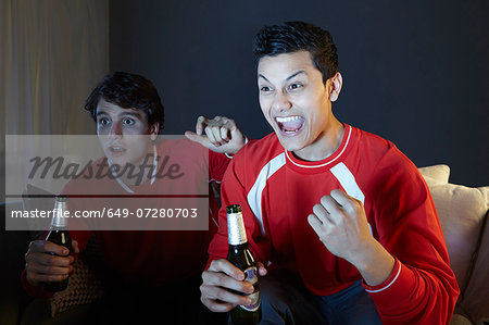 Young men watching sport on tv, holding beer bottle